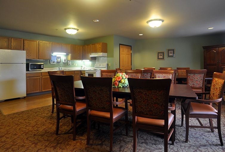 A cozy dining area connected to a kitchen, featuring a large table surrounded by chairs and warm lighting.