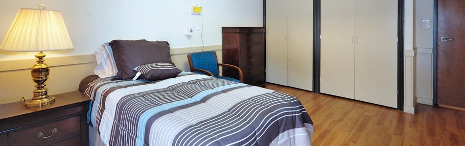 A cozy bedroom with patterned bedding, an armchair, and a wardrobe.