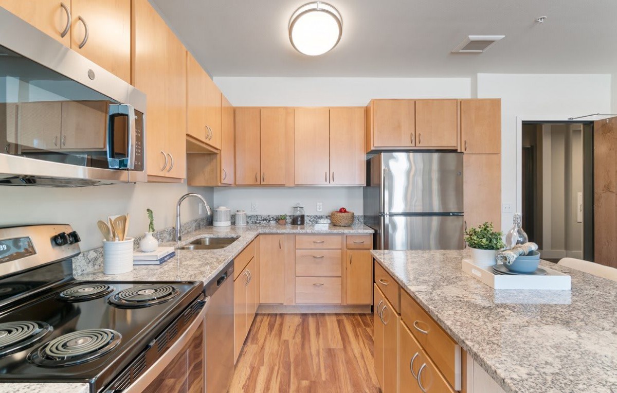 A modern kitchen featuring wood cabinets, stainless steel appliances, and wood flooring.