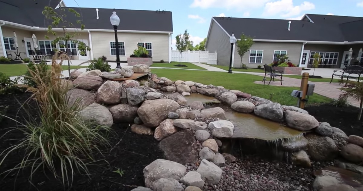 A beautifully landscaped backyard with a rock-lined pond and adjacent houses.