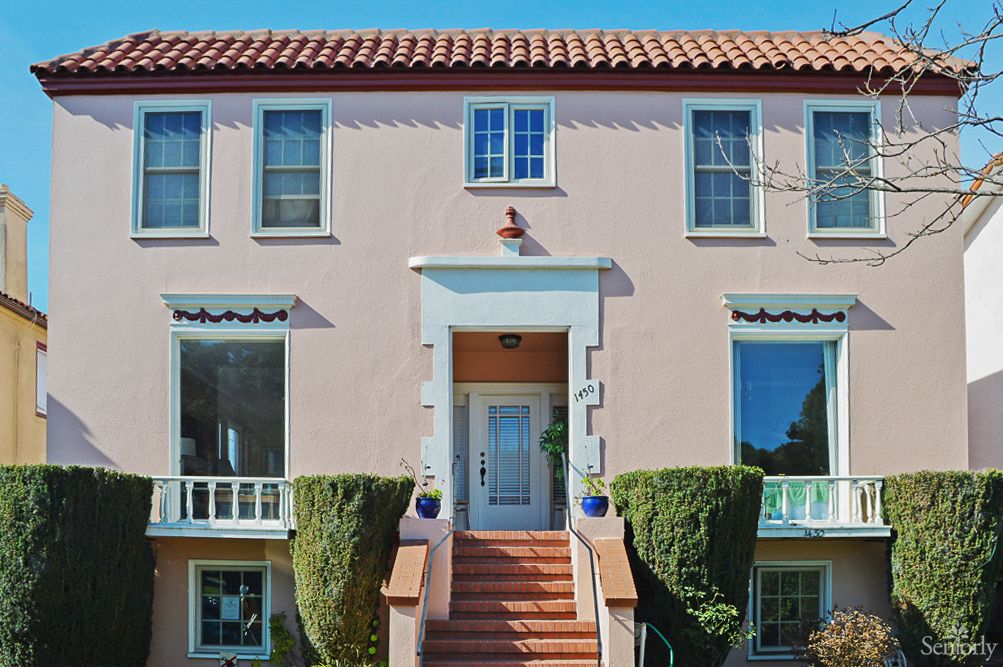 A charming house with a tiled roof and neatly trimmed bushes flanking the entrance stairs.