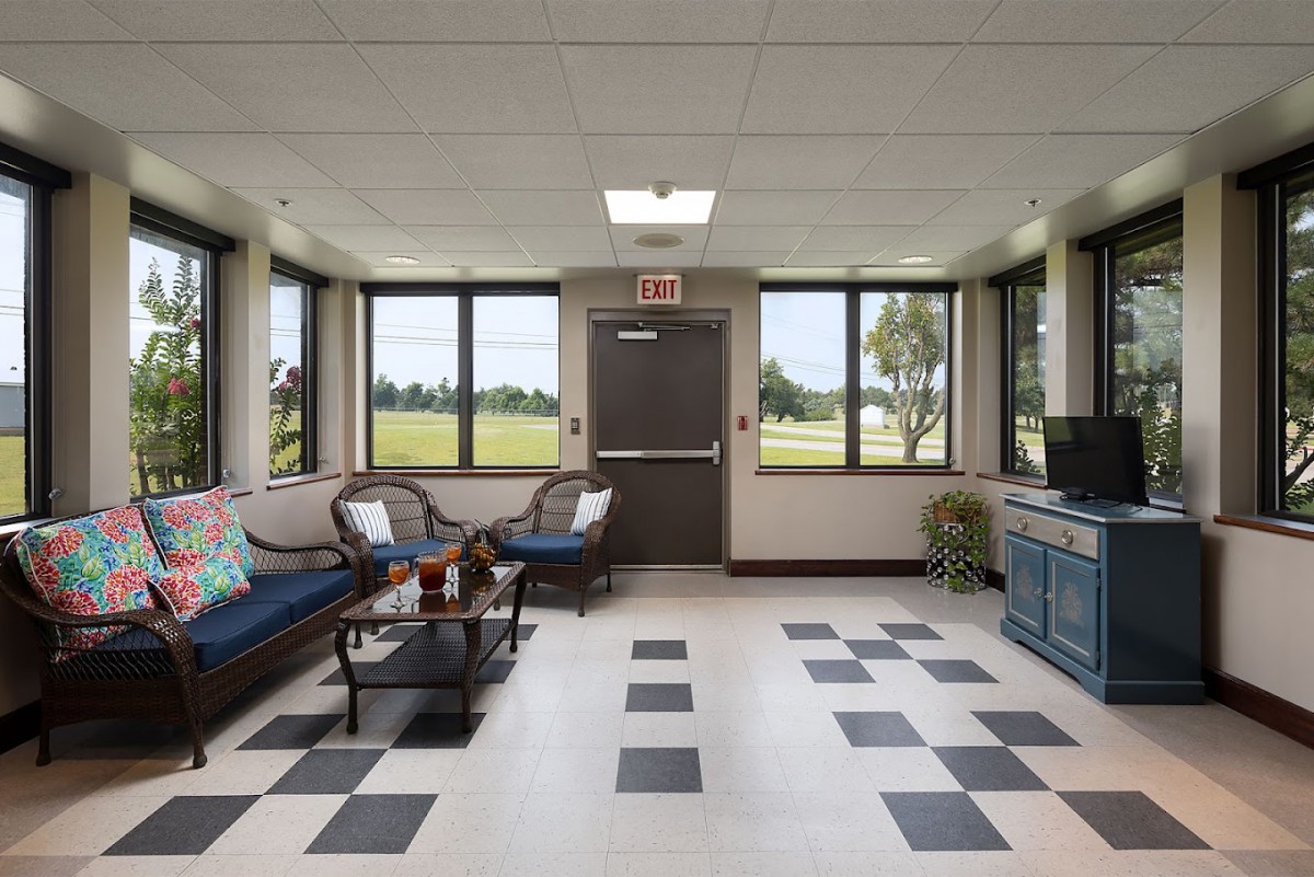 A bright and inviting waiting room featuring several chairs, a coffee table, large windows, and a TV stand.