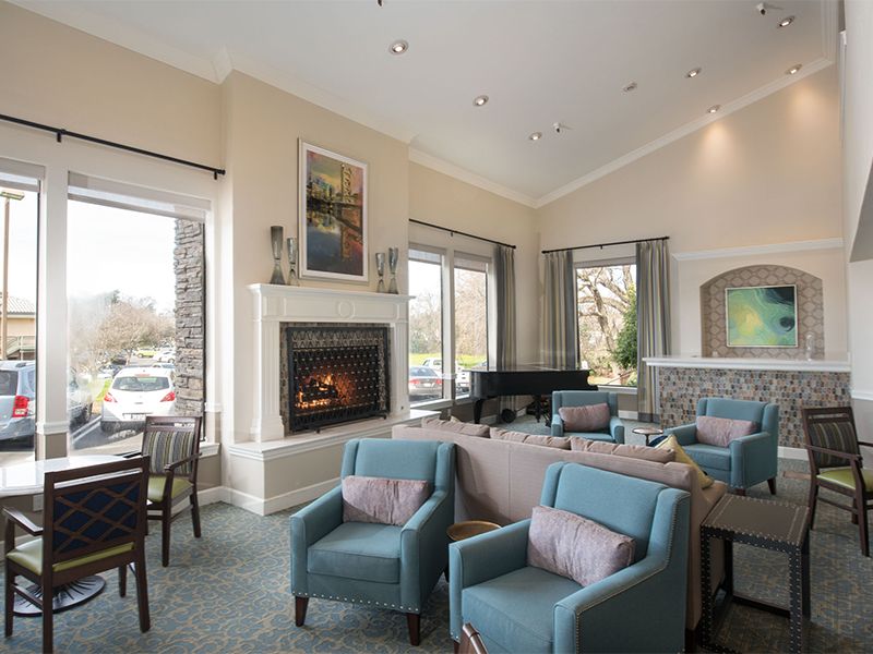 A cozy living room with a fireplace, blue chairs, and large windows.