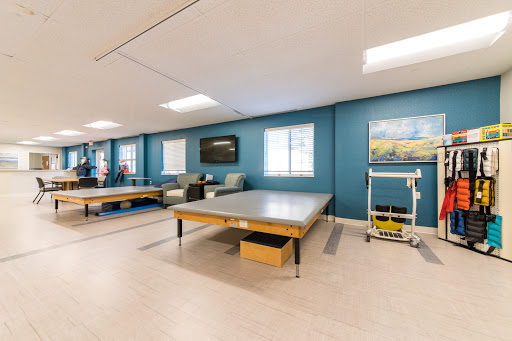 A well-lit therapy room featuring modern tables and calming artwork, designed for rehabilitation purposes.