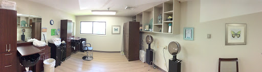 A spacious interior room featuring wooden flooring and various furniture pieces, including shelving and a fan.