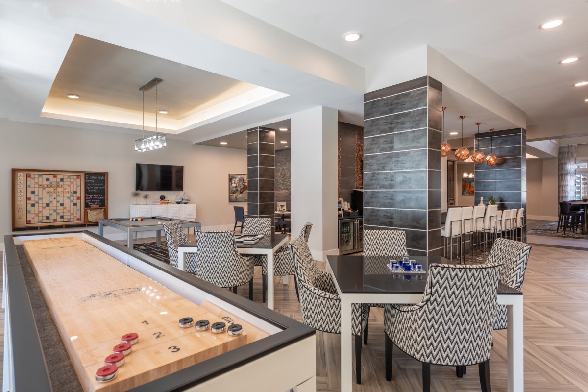 A modern game room featuring a shuffleboard table and comfortable seating.