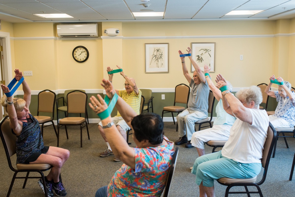 A group of seniors participating in an exercise class using fitness bands indoors.