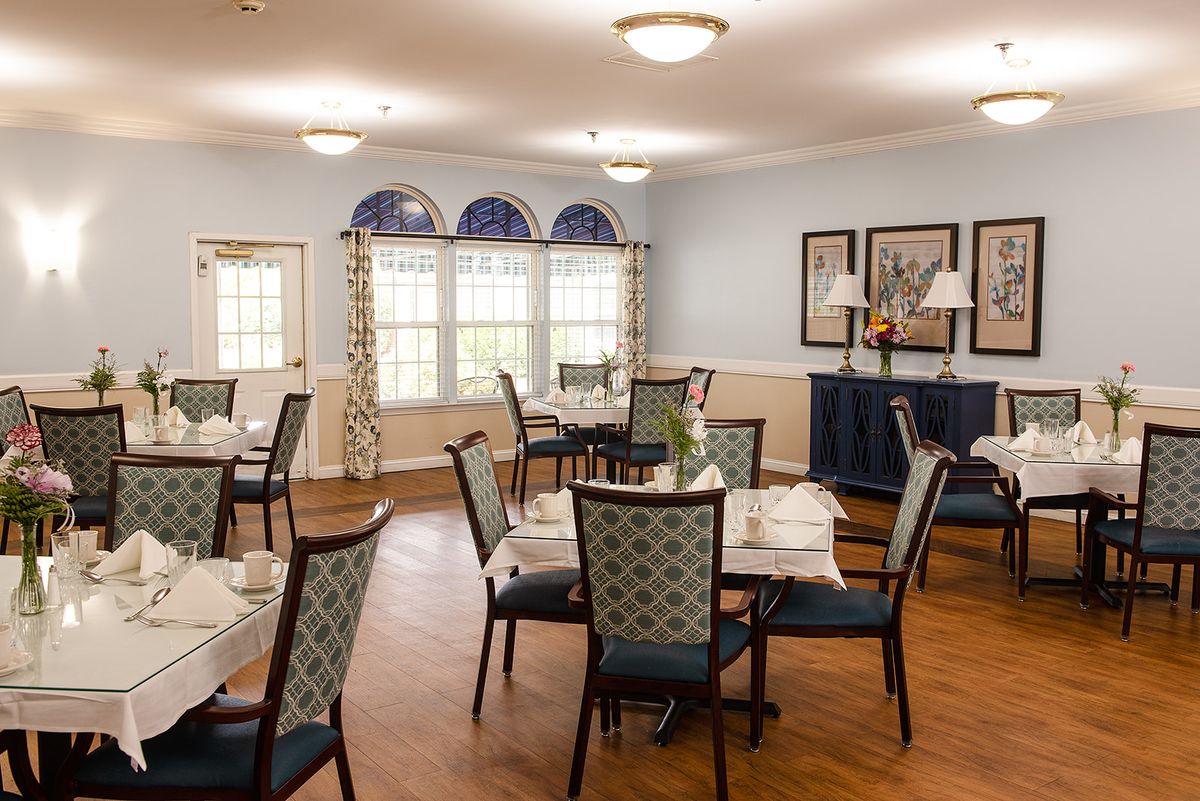 A cozy dining room with neatly arranged tables and chairs, featuring soft lighting and decorative elements.