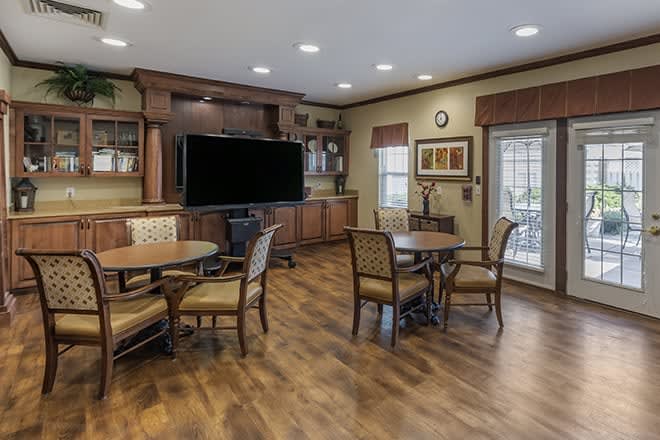 A cozy living room with tables, chairs, and a large television on a wooden floor.