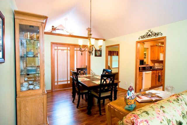 A cozy dining room with a wooden table and chairs, featuring a chandelier and a view into the kitchen.