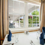 A neatly set dining table by a window, offering a pleasant view outside.