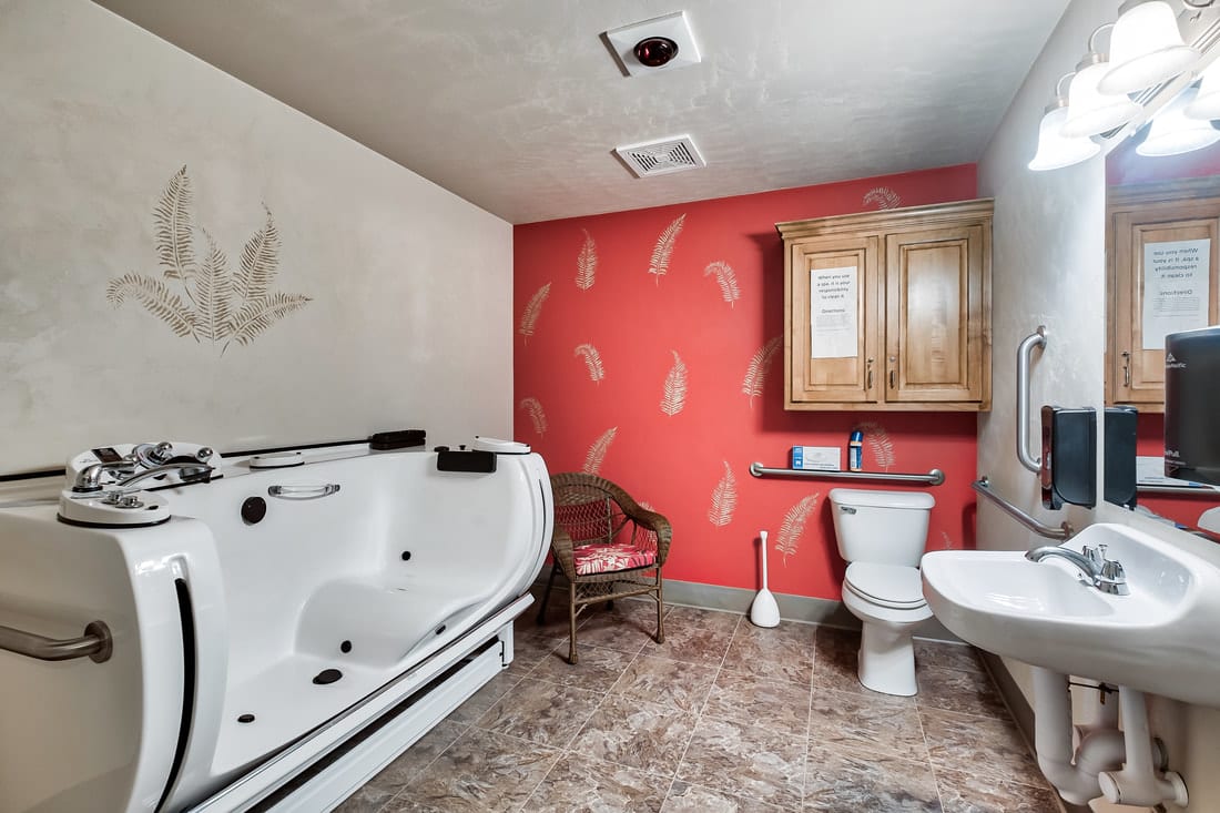 A bathroom featuring a walk-in bathtub, toilet, and sink, accented by red wallpaper and a wooden cabinet.