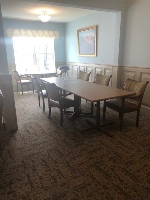 A well-lit conference room with a long table and surrounding chairs, featuring a window and carpeting.