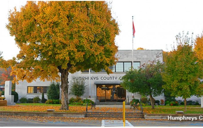 A county office building surrounded by autumn foliage with a flagpole at the entrance.