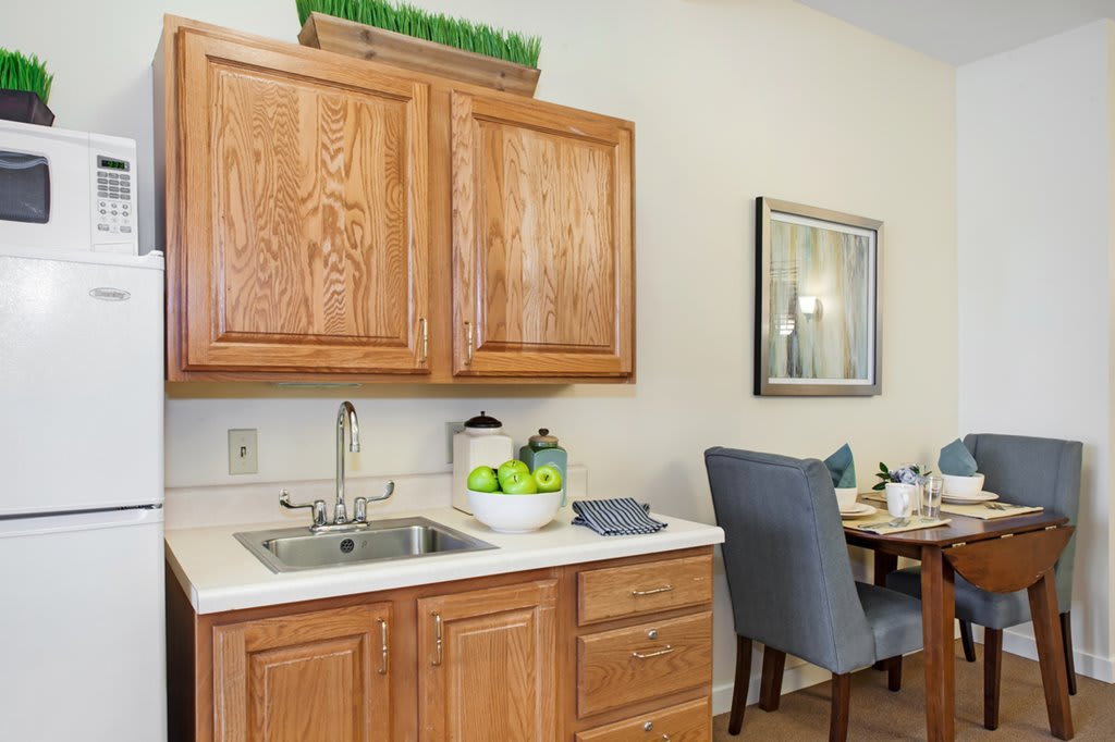 A cozy kitchen corner with wooden cabinets, a sink, and a dining area featuring a set table and comfortable chairs.