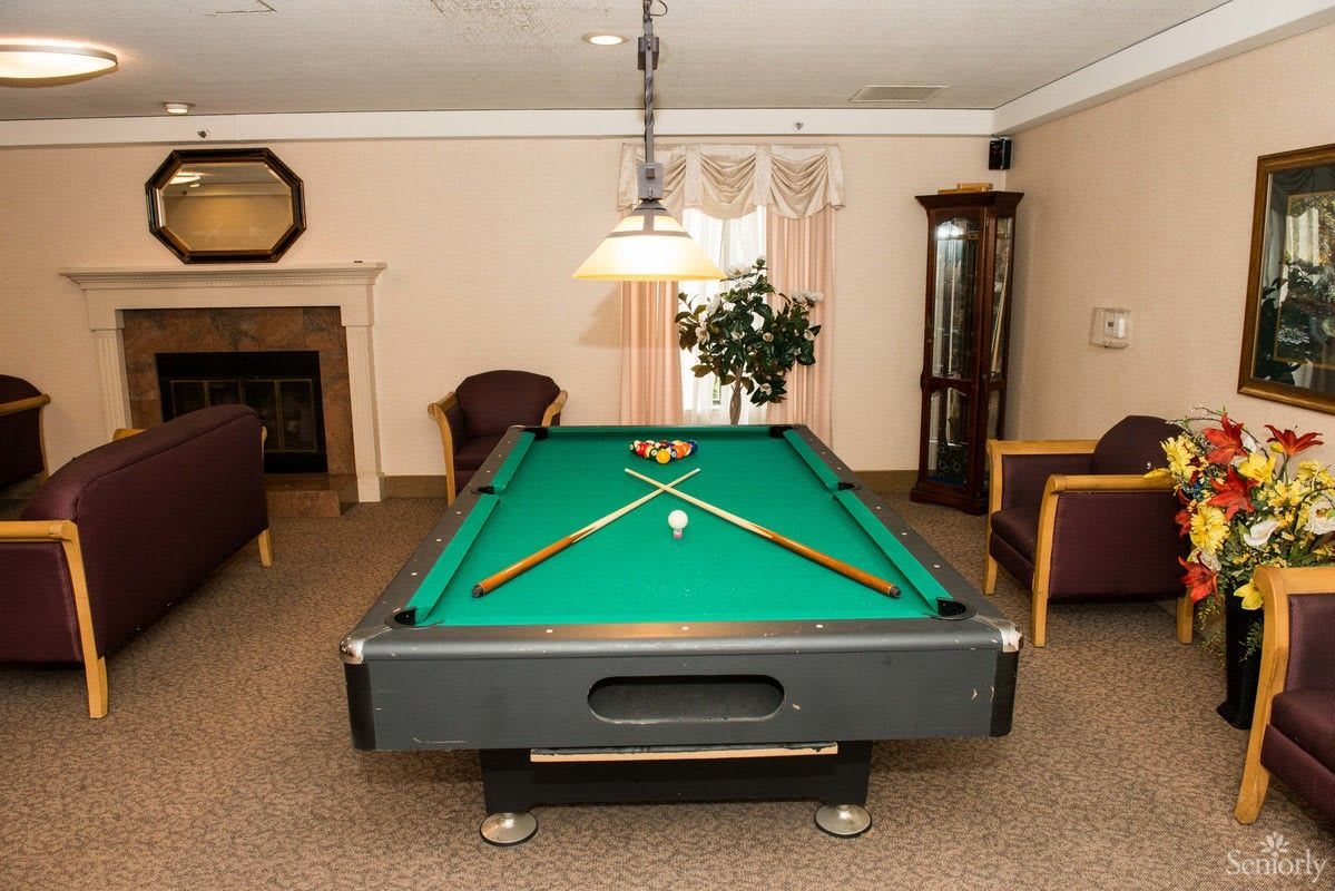 A billiards table in a cozy indoor gaming room with chairs and a lamp overhead.