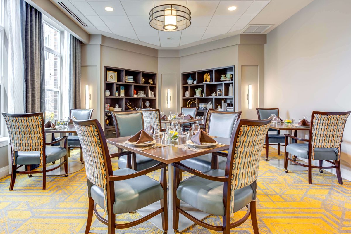 An elegantly furnished dining area with neatly set tables and bookshelves in the background.