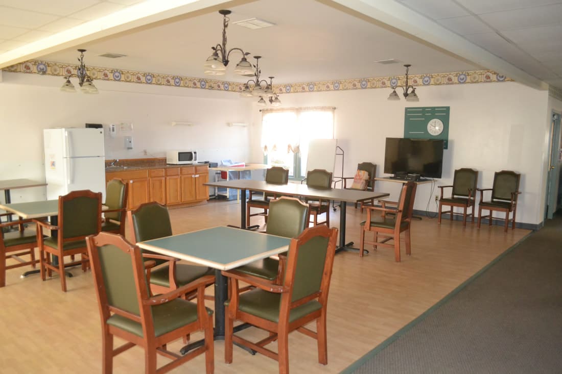 A community room with tables, chairs, a kitchenette, and a television.