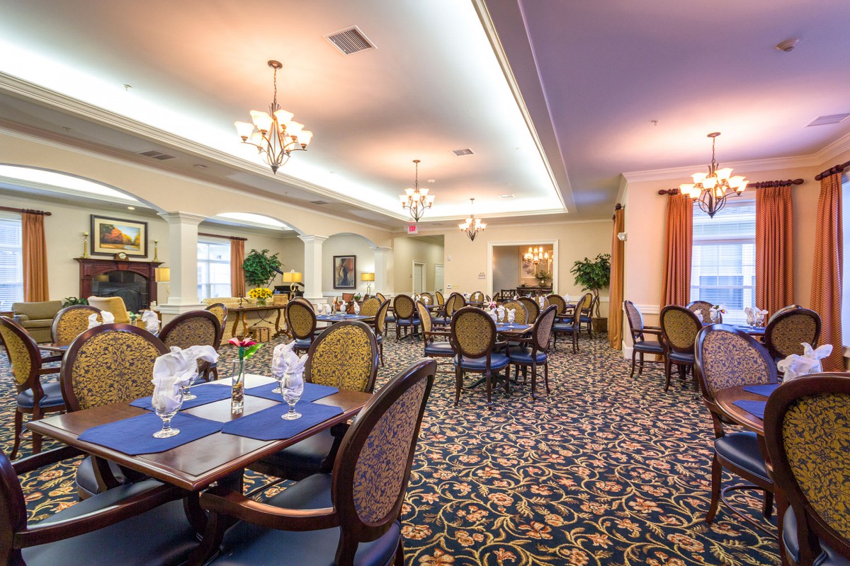An elegant dining room with neatly set tables and chandeliers overhead.