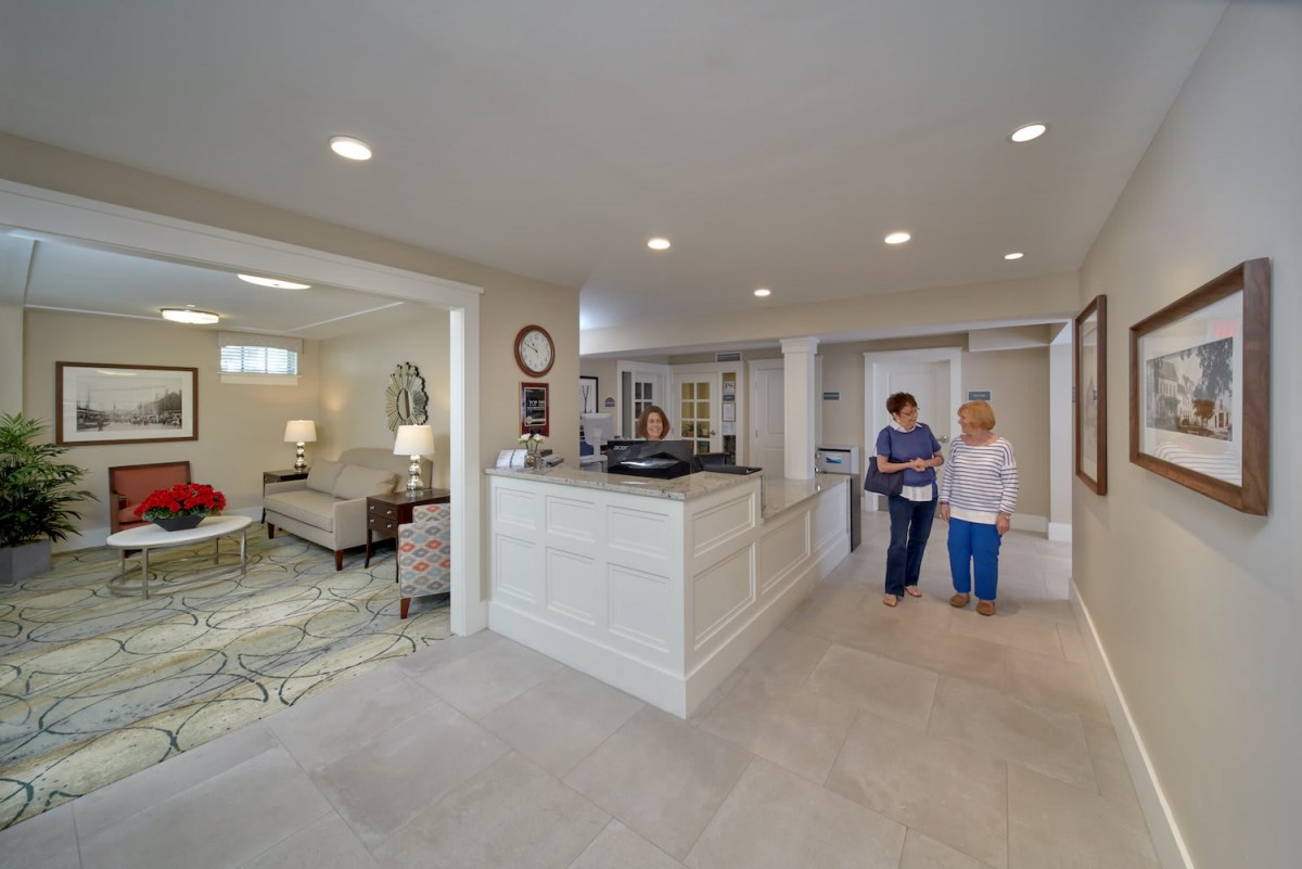 A spacious reception area with modern furnishings and warm lighting, featuring a seating area and people interacting.