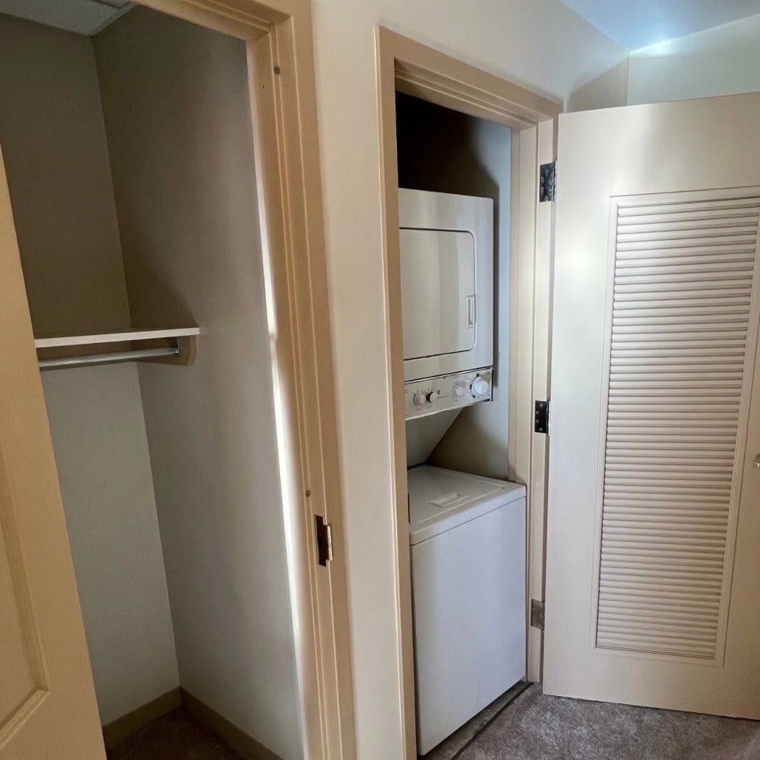 A compact laundry area with a stacked washer and dryer next to an open closet.