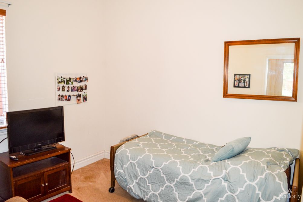 A minimalist bedroom with a single bed and a small television on a stand.