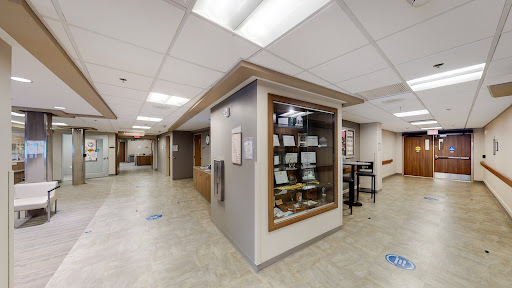A modern interior view of a hospital corridor, featuring a display case and seating areas.