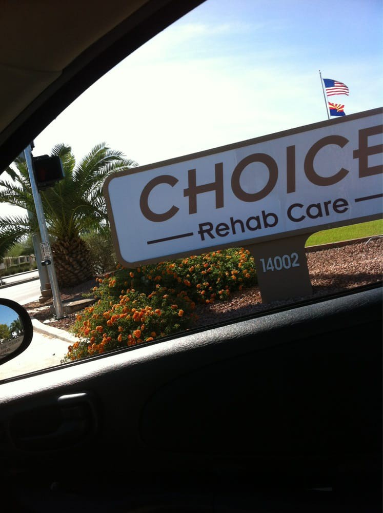 View from a car window of a sign for Choice Rehab Care with palm trees in the background.