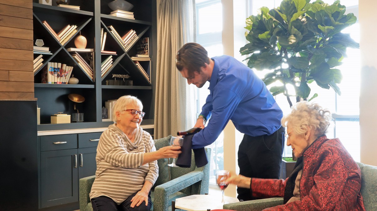 A caregiver assisting elderly individuals with drinks in a communal setting.