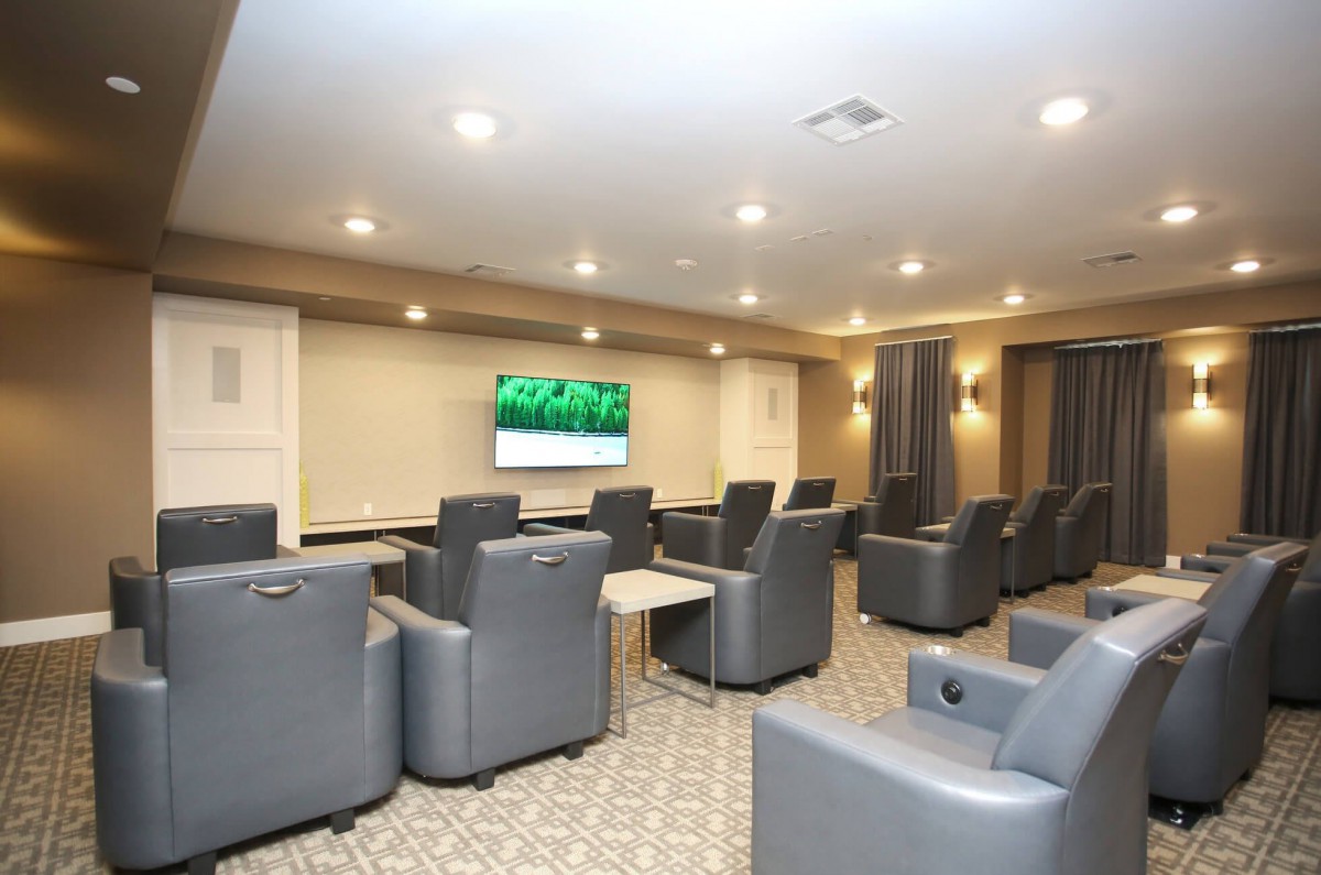 A modern theater room with comfortable recliner chairs facing a large television.