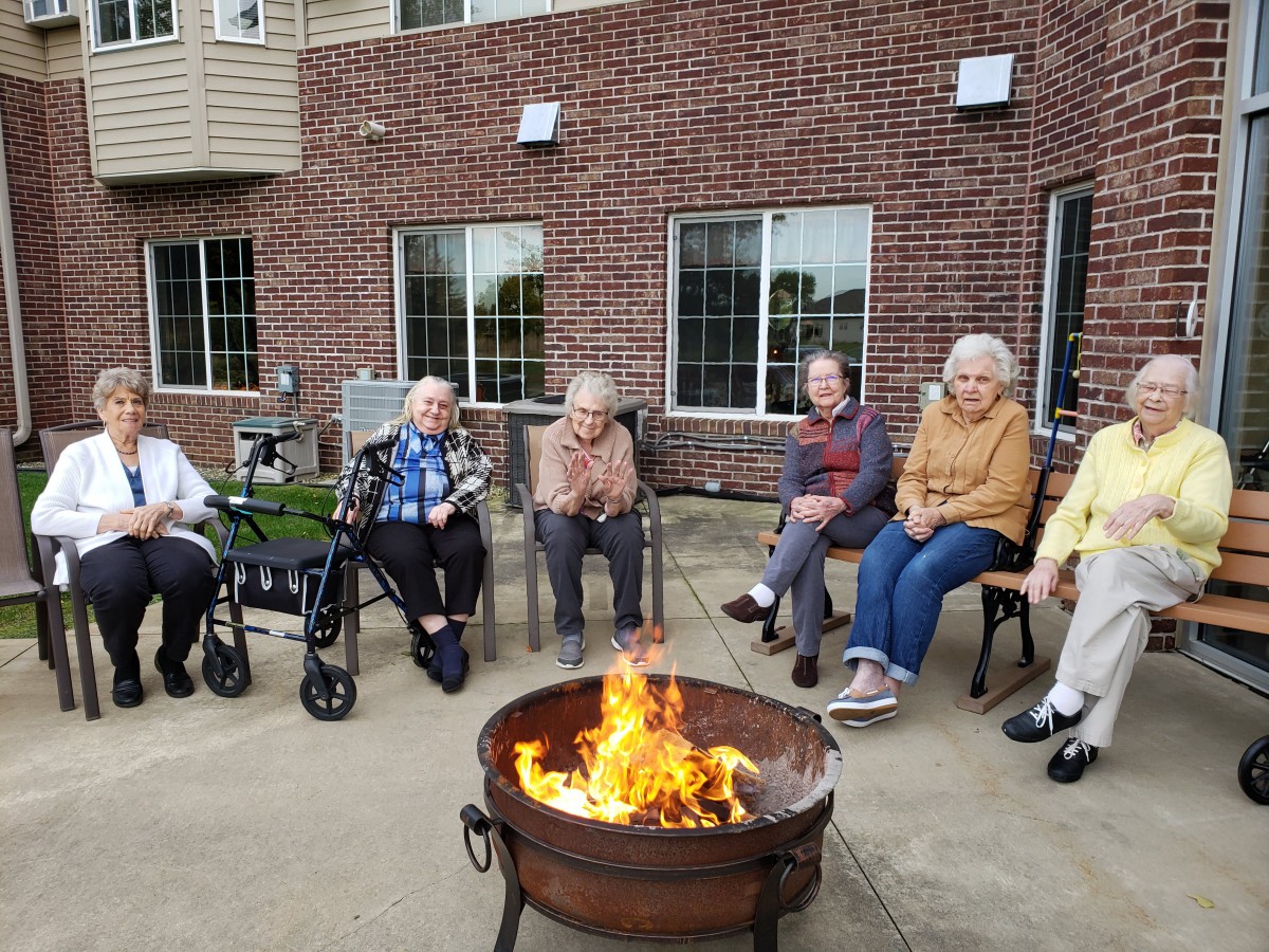 A group of elderly people sitting around a fire pit outside a brick building.