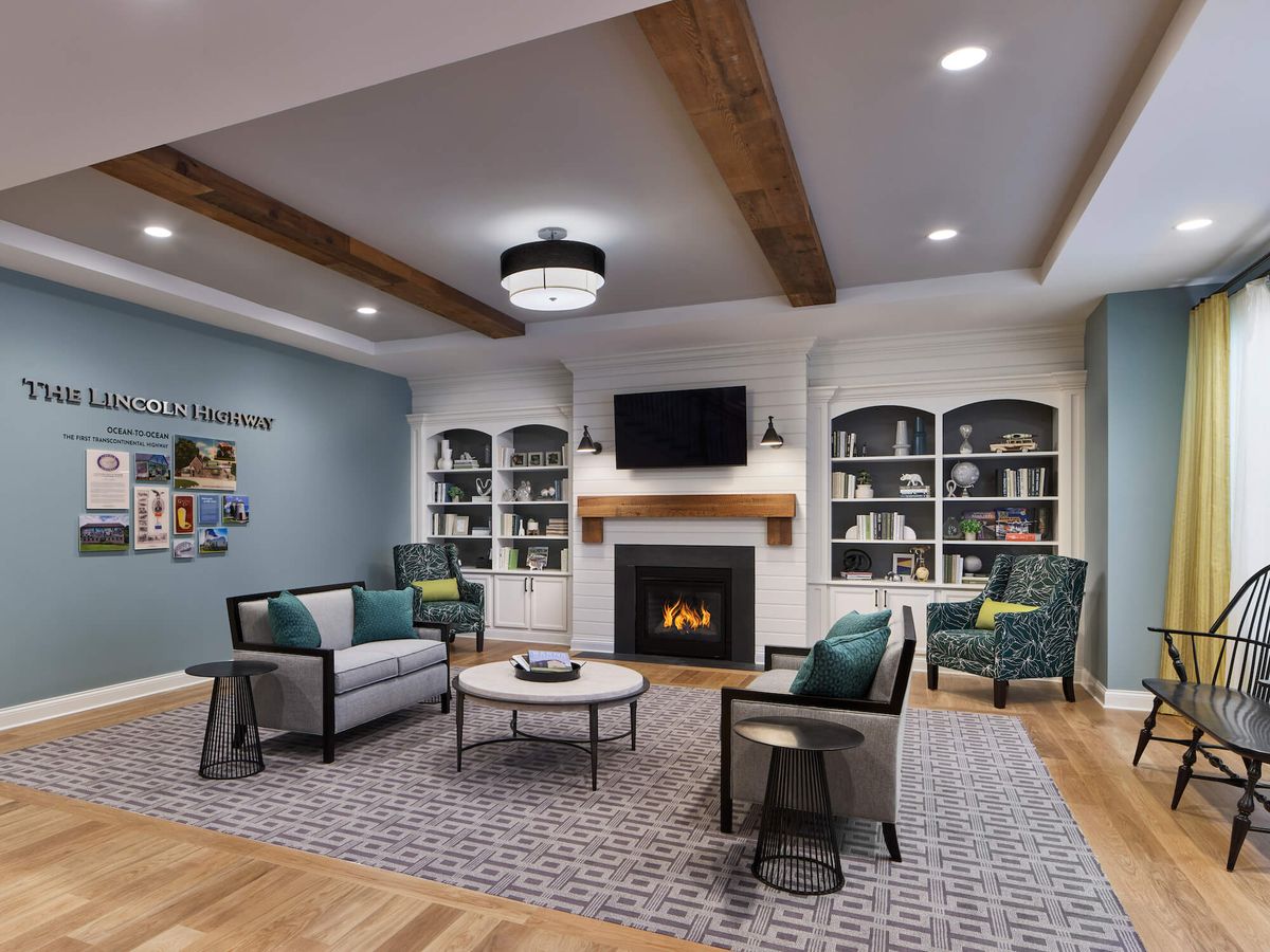 A modern living room featuring a fireplace flanked by bookshelves, comfortable seating, and decorative wood ceiling beams.