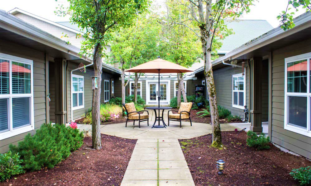 A serene courtyard with outdoor seating and a large umbrella, surrounded by trees and landscaped paths.