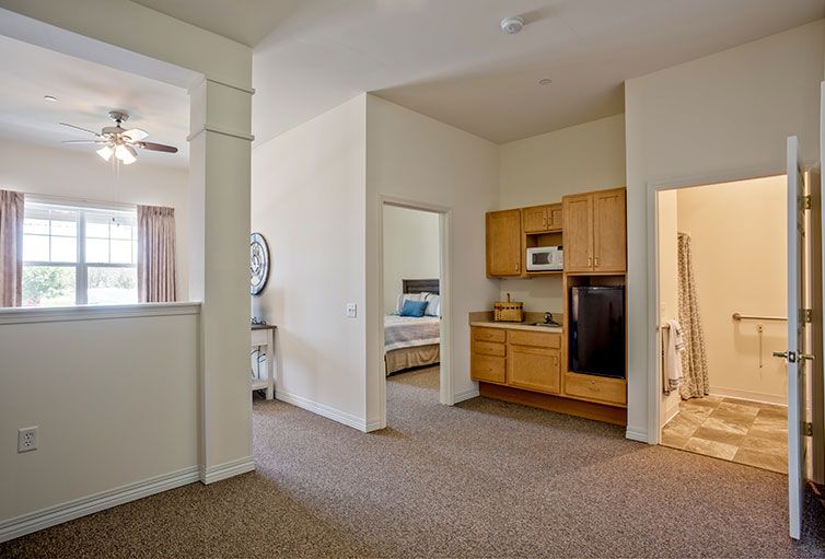 A spacious apartment interior featuring a living area, kitchenette, and adjacent bedroom.