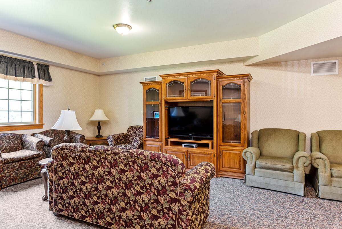 A cozy living room with floral-patterned sofas, an armchair, and a wooden entertainment center holding a television.