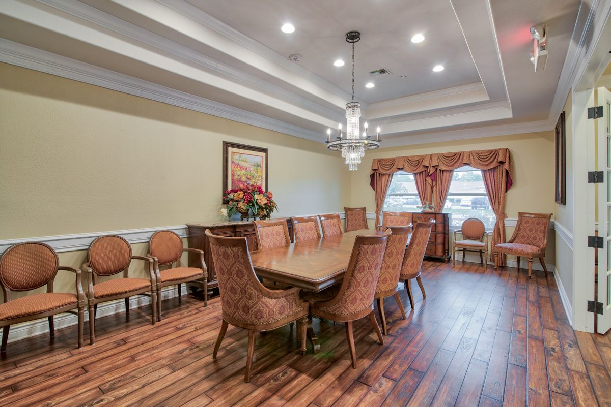 A well-decorated dining room with a large table and elegant chairs, featuring a chandelier and wooden flooring.