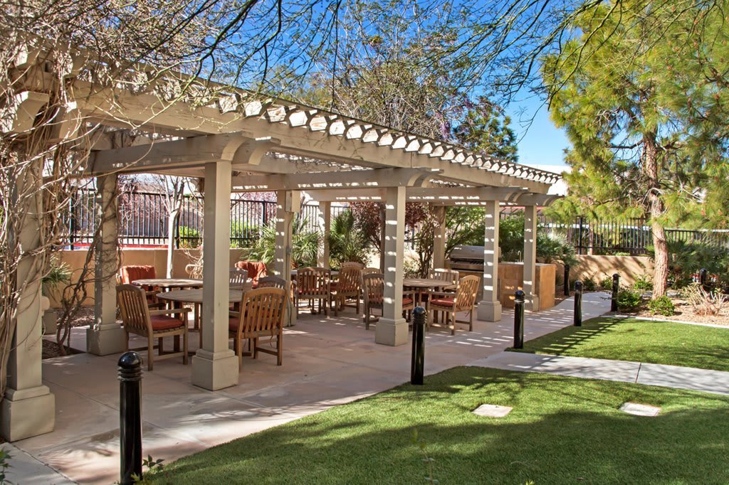 An outdoor seating area under a pergola, surrounded by a garden setting.