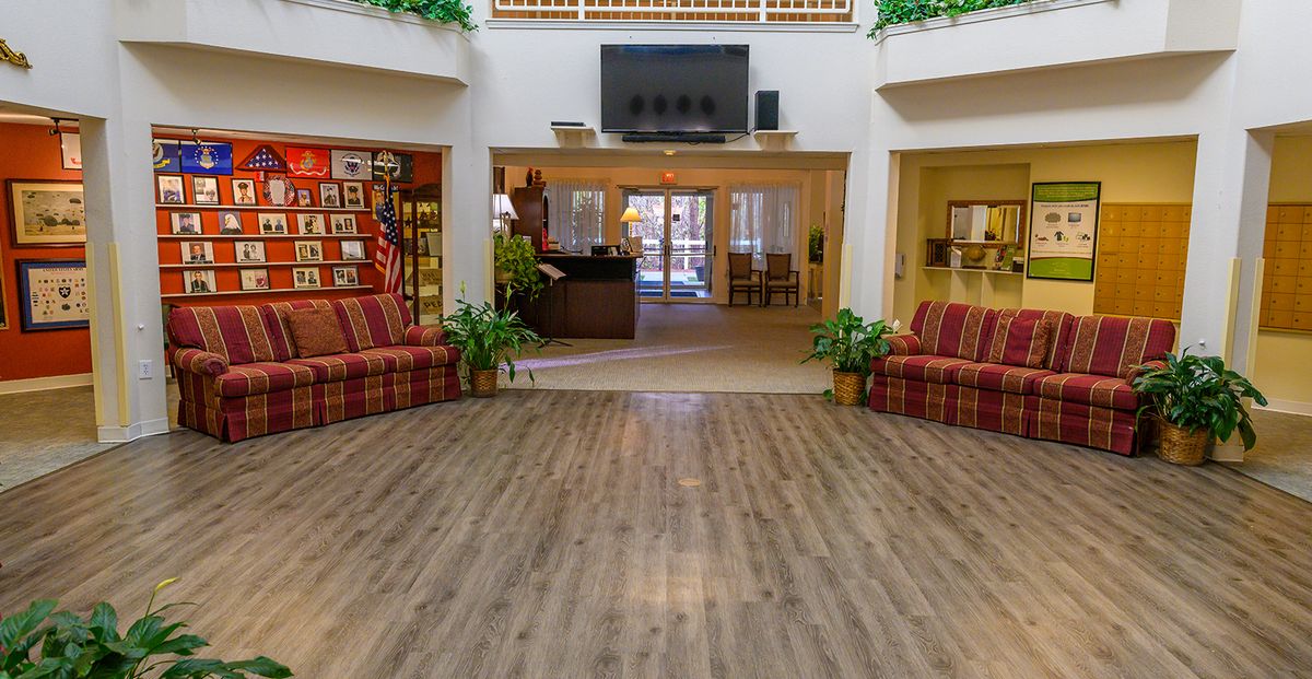 A spacious lobby with wooden flooring, featuring comfortable sofas and decorative plants.