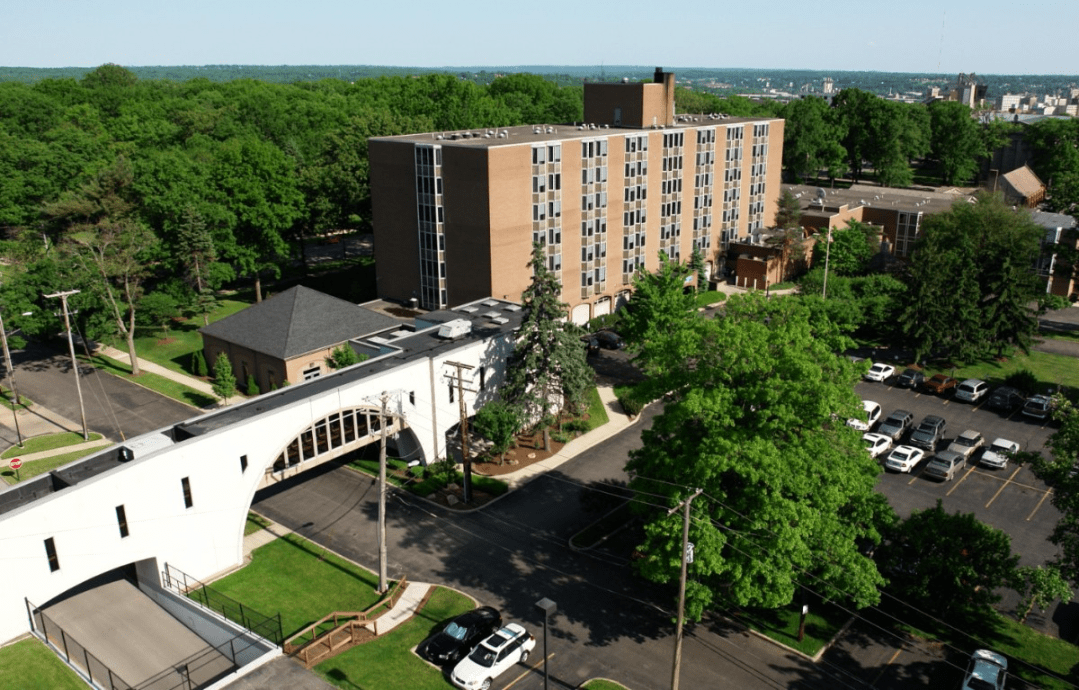 An aerial view of a building surrounded by trees and cars on the road.