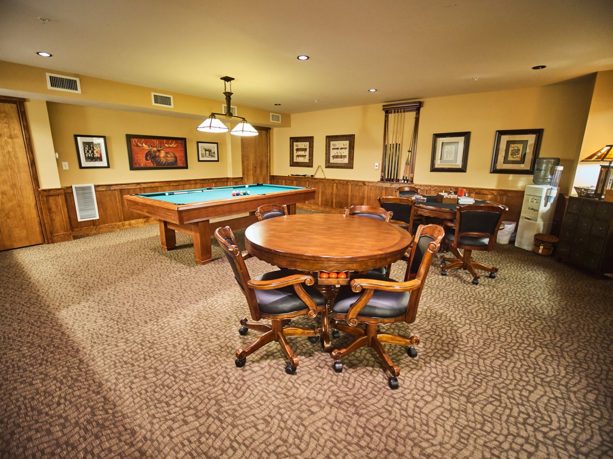 A cozy game room featuring a pool table and a poker table surrounded by chairs, decorated with framed paintings.