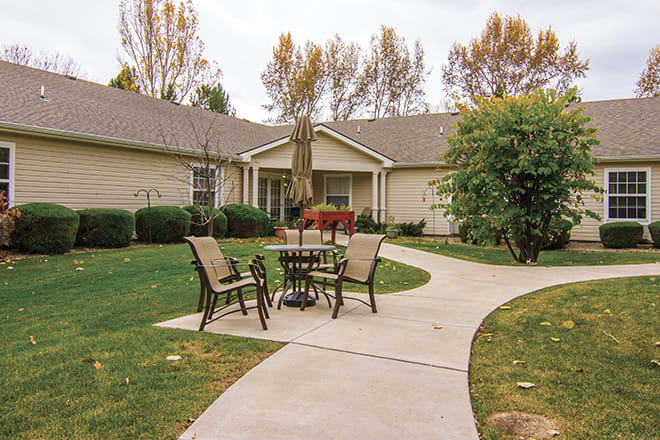 A cozy outdoor patio with a table and chairs set in a garden in front of a house.