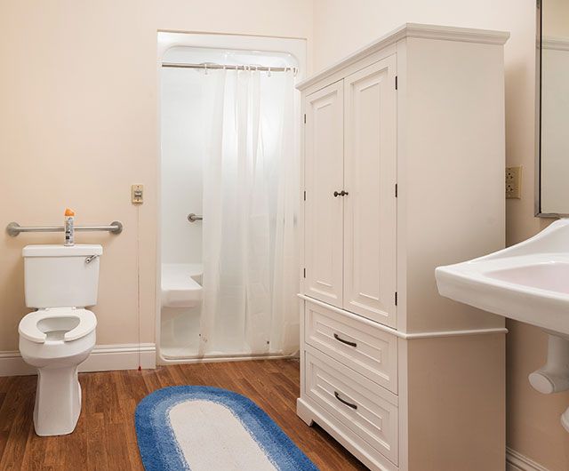 A bathroom featuring a toilet, cabinet, sink, and shower with a wooden floor.