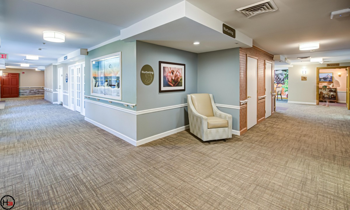 A well-lit hallway featuring a comfortable chair and artwork on the wall.
