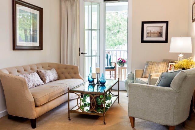 A cozy living room featuring a beige sofa, armchair, and decorative coffee table with natural light streaming in through the window.