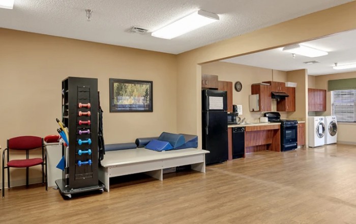A view of a home interior featuring a living area with exercise equipment and an adjacent kitchen.