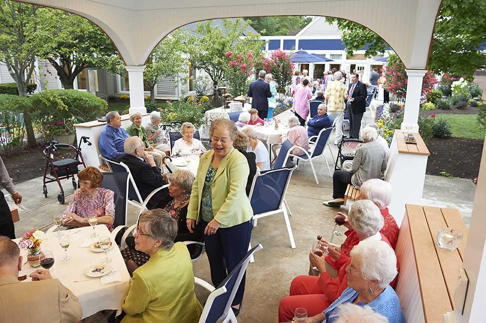 A lively outdoor gathering of seniors enjoying a social event under a covered patio.