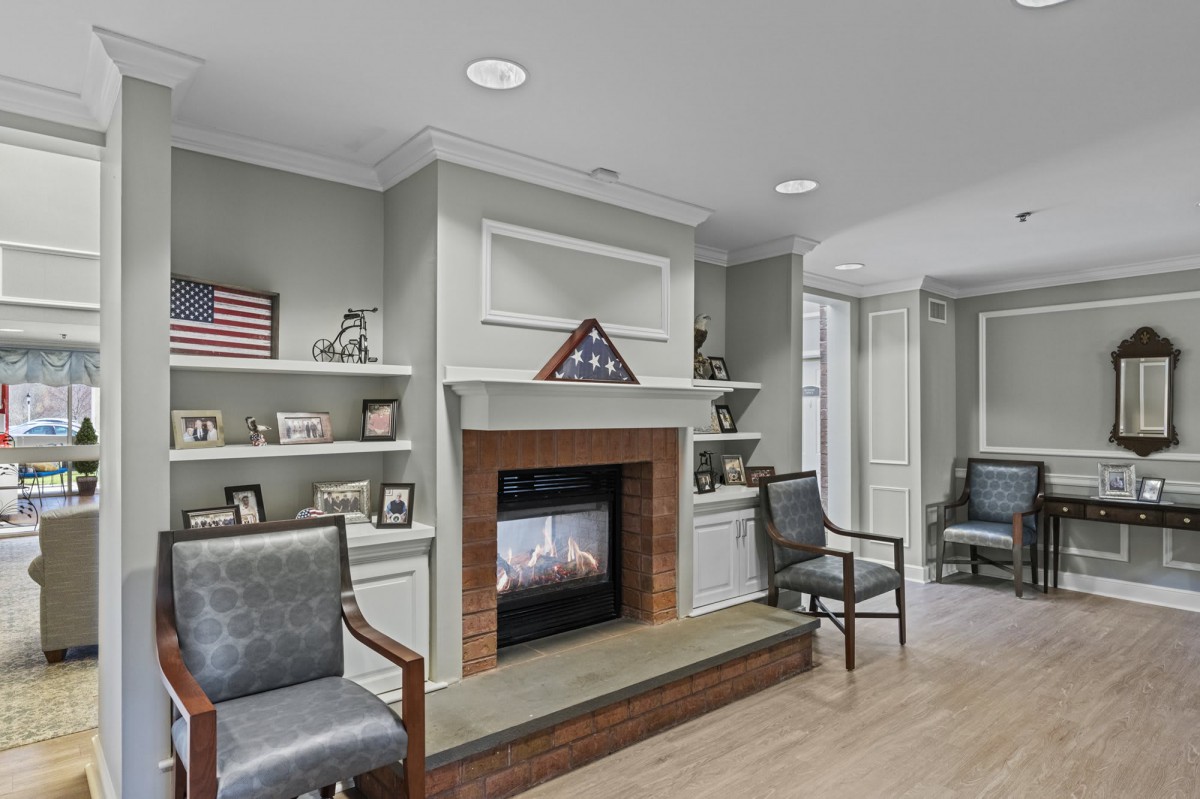 A cozy living room with a fireplace, chairs, and decorated bookshelves.