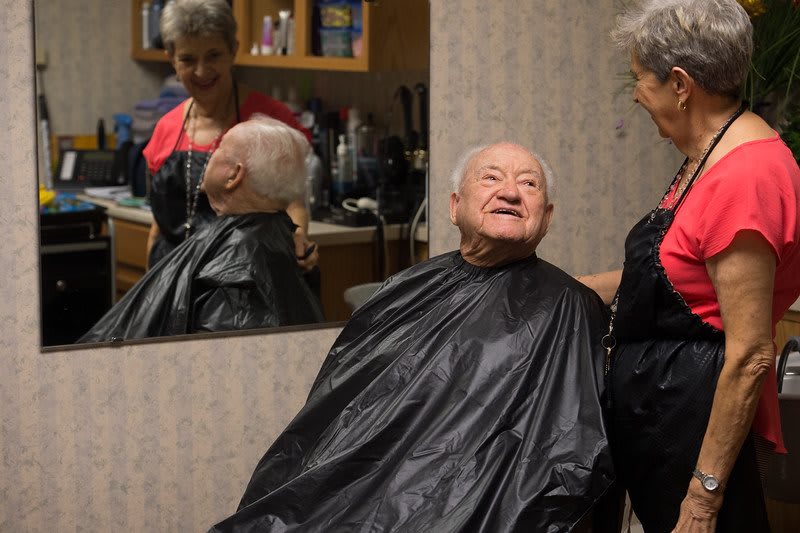 An elderly man smiles while getting a haircut in a salon.