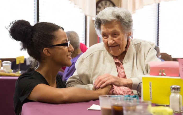A young woman and an elderly woman share a warm conversation at a table.
