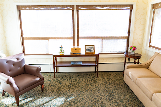 A cozy living room featuring a brown armchair, beige sofa, and a coffee table positioned near large windows that let in plenty of natural light.